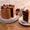 A multi-layered chocolate cake with buttercream, topped with rosettes, truffles, and chocolate chunks, alongside a slice on a plate with coffee.