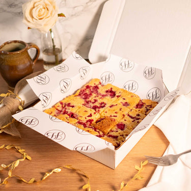 Box of White Chocolate and Raspberry Blondies with a mug, a rose and a fork