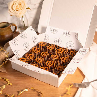 Box of Salted Caramel Brownies with pretzels and caramel drizzle, next to a mug