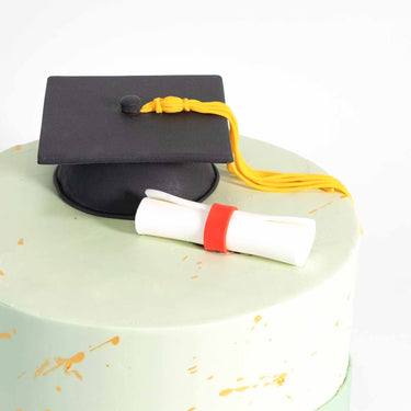 Graduation Cake with pale green buttercream, gold splatters, a fondant graduation cap and scroll