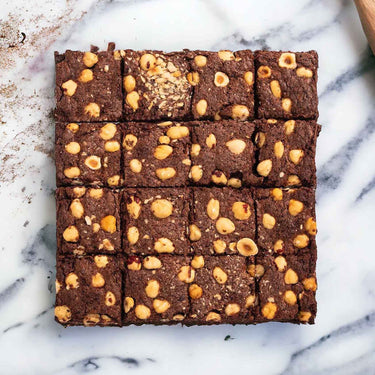 16 Chocolate and Hazelnut Brownies topped with whole hazelnuts, on marble