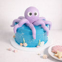 Mini Under The Sea Cake with blue buttercream and a purple fondant octopus, next to shell shaped biscuits