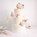 Rustic Wedding Cake with white buttercream, pink roses and greenery, on a table with champagne and macarons