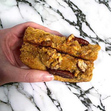 Hand holding a pecan and caramel cookie broken in half, on marble