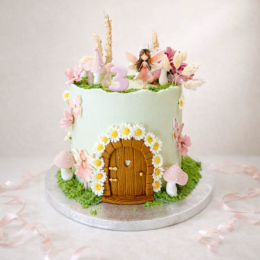 Fairy house cake with a wooden door, daisies and a fairy on top