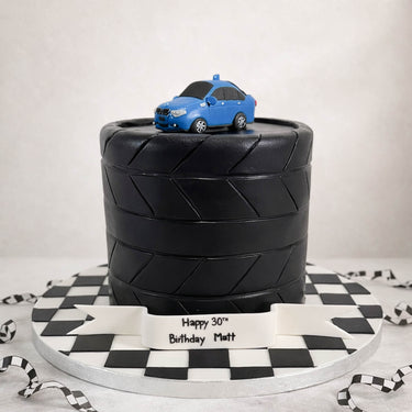 Car tyre cake with a blue car on top and a chequered flag board