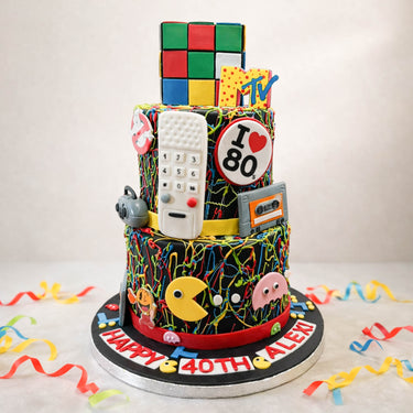 Two tier 1980s themed 40th birthday cake with a Rubik's cube and Pac-Man