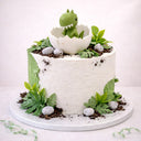 Free From Baby Dino Cake with textured buttercream, edible soil, sweet pebbles and a dinosaur hatching from an egg