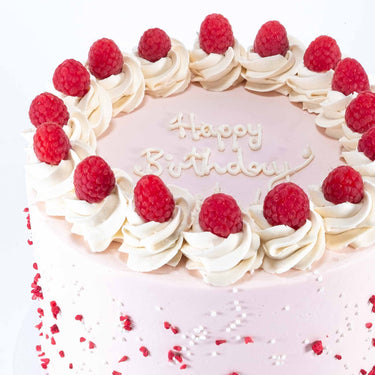 Raspberry White Chocolate Cake topped with cream rosettes, fresh raspberries, sugar pearls and sprinkles