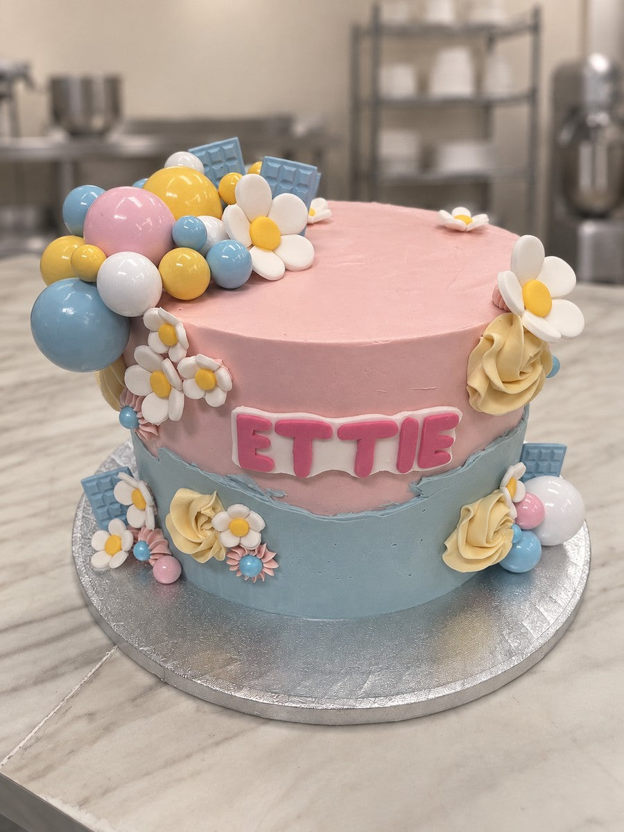 Pink and blue buttercream birthday cake with white daisies, pastel balls, cream roses and ETTIE in pink letters