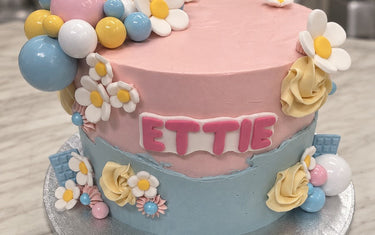 Pink and blue buttercream birthday cake with white daisies, pastel balls, cream roses and ETTIE in pink letters