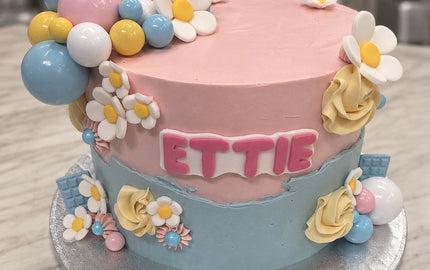 Pink and blue buttercream birthday cake with white daisies, pastel balls, cream roses and ETTIE in pink letters