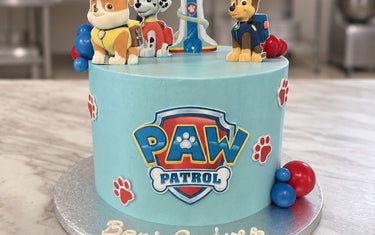 Pale blue Paw Patrol birthday cake with Chase, Marshall and Rubble toppers, the lookout tower and red paw prints