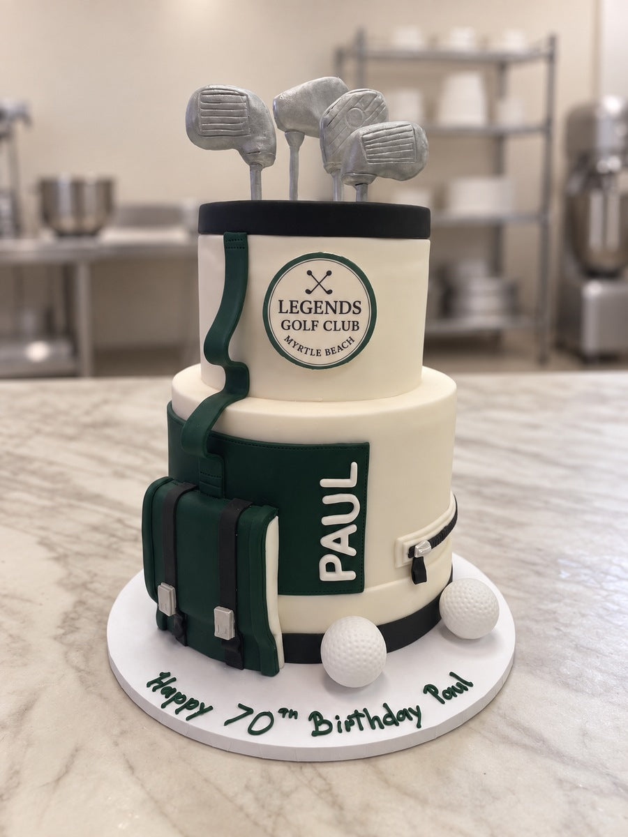 Two-tier golf bag birthday cake in cream, green and black with sugar golf clubs, golf balls and PAUL on the pocket