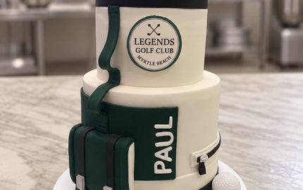 Two-tier golf bag birthday cake in cream, green and black with sugar golf clubs, golf balls and PAUL on the pocket