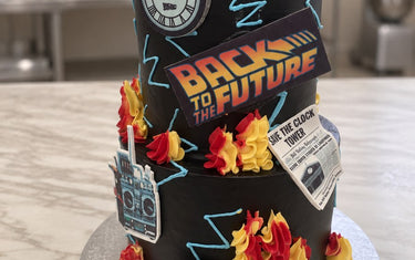 Black two-tier Back to the Future birthday cake with DeLorean topper, red and yellow buttercream flames and a 15:38 clock