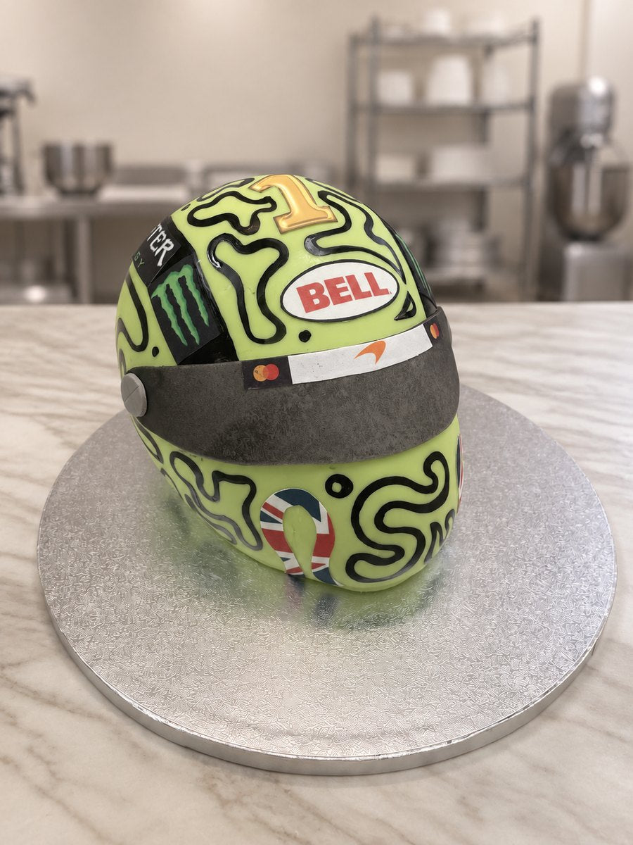 Carved lime green F1 racing helmet cake with black swirl pattern, dark visor and gold number one on a silver board