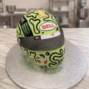 Carved lime green F1 racing helmet cake with black swirl pattern, dark visor and gold number one on a silver board