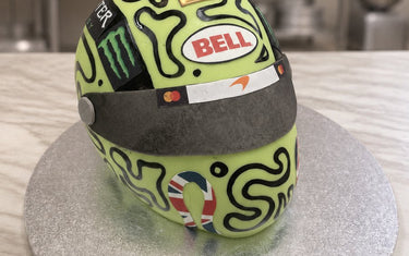Carved lime green F1 racing helmet cake with black swirl pattern, dark visor and gold number one on a silver board