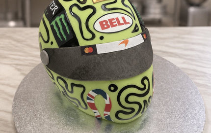 Carved lime green F1 racing helmet cake with black swirl pattern, dark visor and gold number one on a silver board