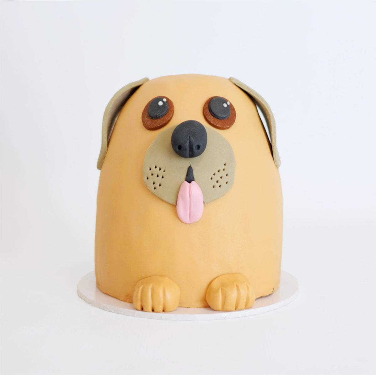 Cartoon-style dog cake with orange fondant, featuring floppy ears, big eyes, snout with tongue, and front paws; a creative novelty by Harry Batten.