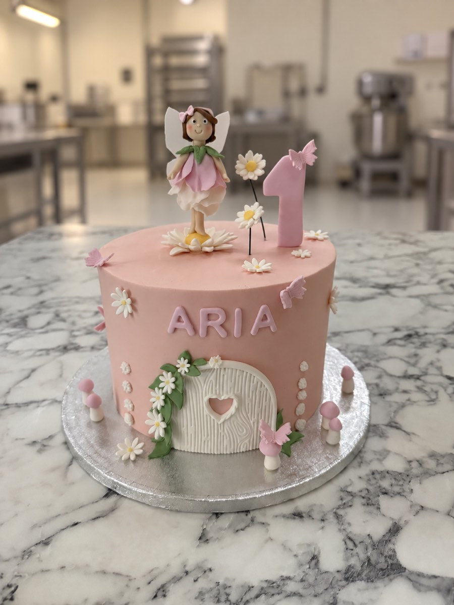 Pale pink fairy first birthday cake with a sugar fairy, number one, white daisies, butterflies, toadstools and a fairy door