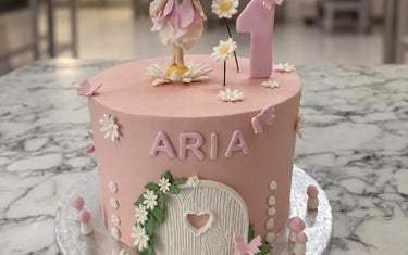 Pale pink fairy first birthday cake with a sugar fairy, number one, white daisies, butterflies, toadstools and a fairy door