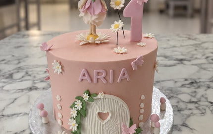 Pale pink fairy first birthday cake with a sugar fairy, number one, white daisies, butterflies, toadstools and a fairy door