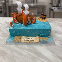 Blue buttercream sea cake with a sugar pirate ship, orange kraken tentacles, a treasure chest island and birthday scroll