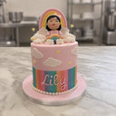 Pink rainbow birthday cake with clouds, stars, pastel stripes, a sugar girl topper holding a rainbow and Lily in pink script