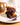 Stack of chocolate brownies on a white plate, drizzled with caramel sauce, accompanied by a silver fork; ceramic mug blurred in the background.