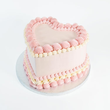Frilly Heart Cake with pale pink icing and pink and ivory piped borders on a silver board