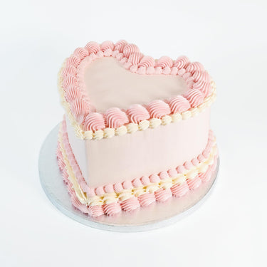 Frilly Heart Cake with pale pink icing and pink and ivory piped borders on a silver board