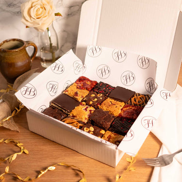 Box of assorted brownies and blondies with a rose and a mug on a wooden table