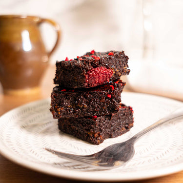 Three chocolate brownies with raspberry pieces on a patterned plate