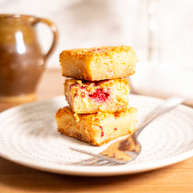 Three blondies with raspberry pieces on a patterned plate