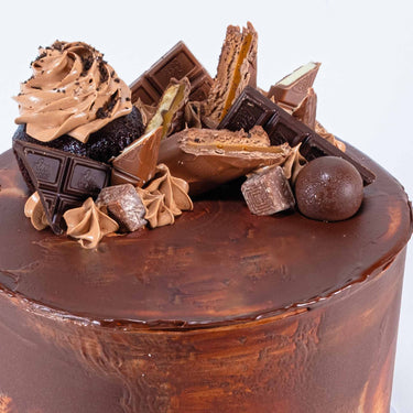 8 inch Chocolate Overload Cake with chocolate buttercream, a cupcake, chocolate bars and truffles on top