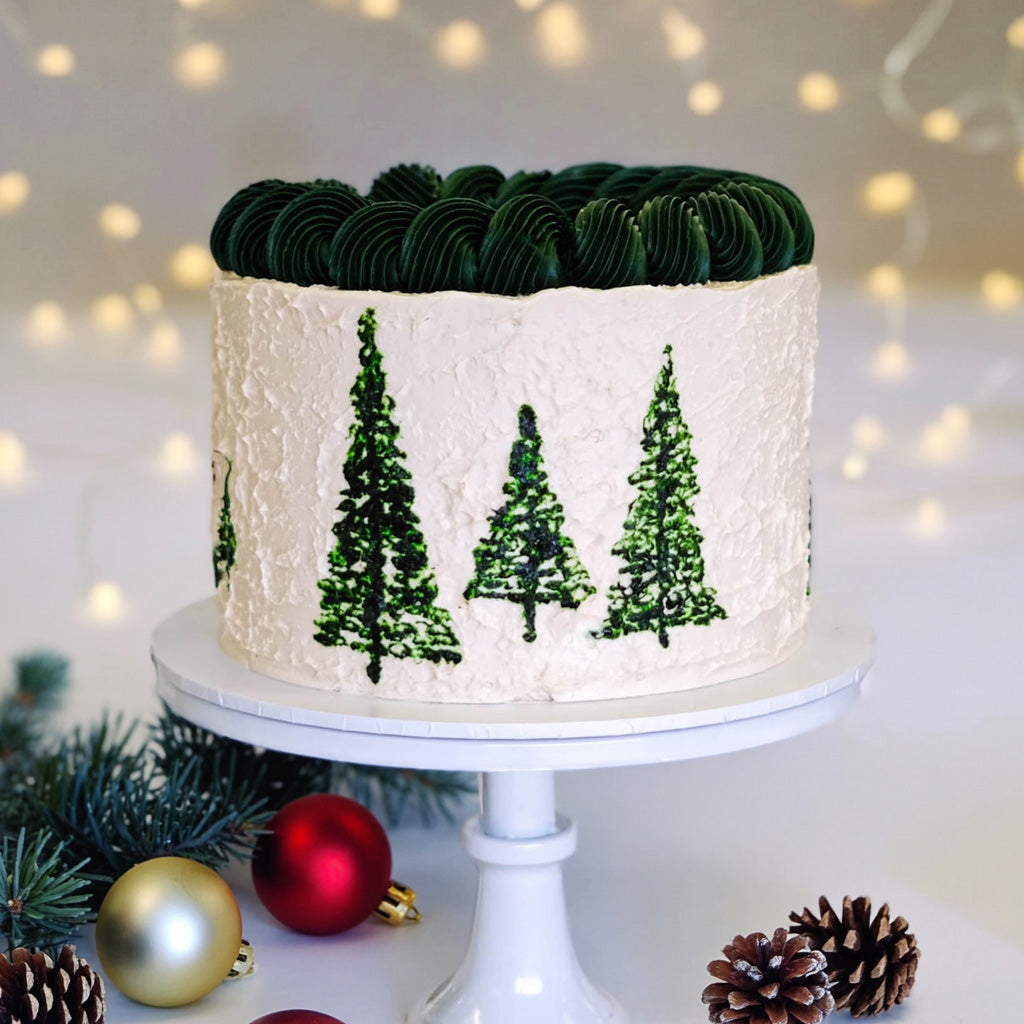 Christmas Tree Cake on a white cake stand with piped buttercream trees and rosettes