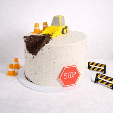 Vegan Free From Digger Cake with a fondant digger, traffic cones and barriers on speckled buttercream