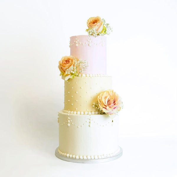 A three-tiered wedding cake with floral decoration, featuring pastel colors and fresh flower embellishments.