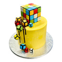 Custom Cake with yellow icing, featuring an edible Rubik’s Cube and colorful fondant cubes. Contact Harry Batten before ordering. Contains allergens; see details.