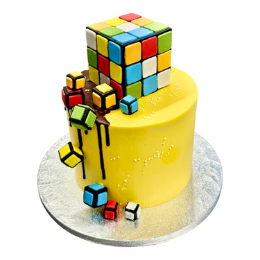 Custom Cake with yellow icing, featuring an edible Rubik’s Cube and colorful fondant cubes. Contact Harry Batten before ordering. Contains allergens; see details.