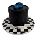 Custom Cake: Tire-themed birthday cake with black fondant, blue toy car, and checkered board. Banner reads “Happy 30th Birthday Matt.” Contact us before purchasing.