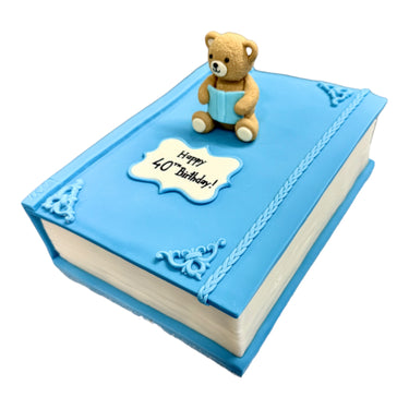Custom Cake: A birthday cake resembling a book with a blue cover, featuring a fondant teddy bear and Happy 40ᵗʰ Birthday! message on a white plaque.