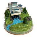 Custom Cake by Harry Batten: A green buttercream hill with a multi-level house and fir-tree confections, featuring a blue fondant waterfall.