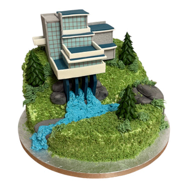 Custom Cake by Harry Batten: A green buttercream hill with a multi-level house and fir-tree confections, featuring a blue fondant waterfall.