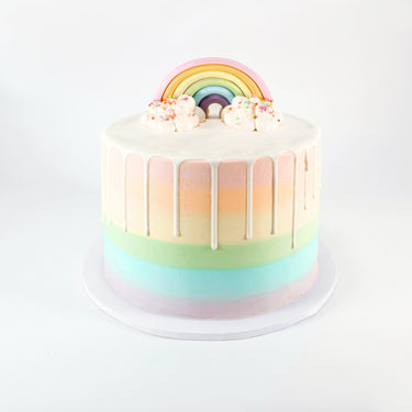 Tall Rainbow Cake with pastel rainbow stripes, white drip and a fondant rainbow with buttercream clouds