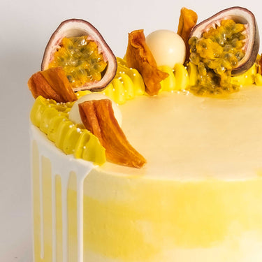 Gluten friendly Free From White Chocolate Passionfruit Cake with yellow buttercream, white drip, passionfruit and mango