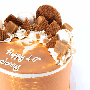 Salted Caramel Cake topped with stroopwafels, fudge and macarons, with a piped birthday message