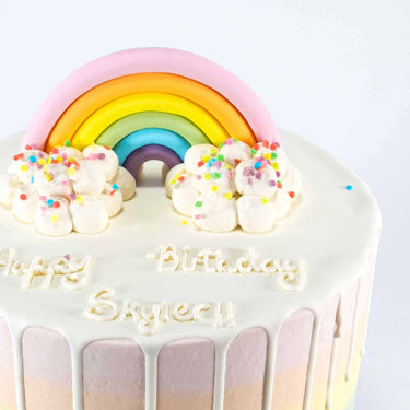 Rainbow Cake with a fondant rainbow, white chocolate drip and a piped happy birthday message